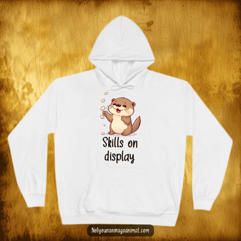 Funny hoodie featuring a curious otter delightedly juggling shiny pebbles, exuding warmth and playful charm.